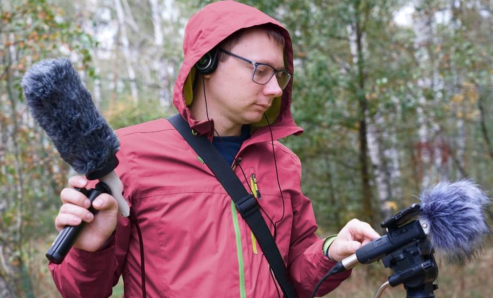 Junger Mann steht mit Mikrofonen im Wald